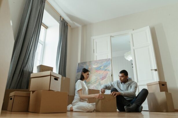 A couple sitting on the floor surrounded by moving boxes.